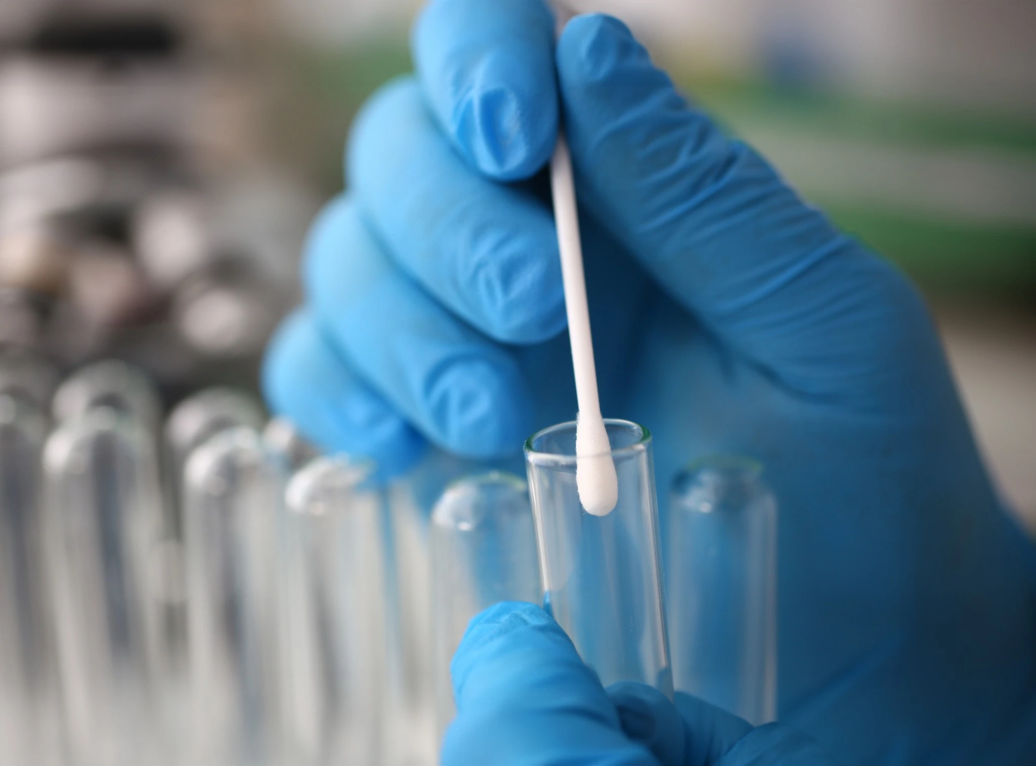 Técnico realizando amostragem por swab em tubo de ensaio, representando etapas de coleta e testes em estudos de validação de limpeza na indústria farmacêutica.