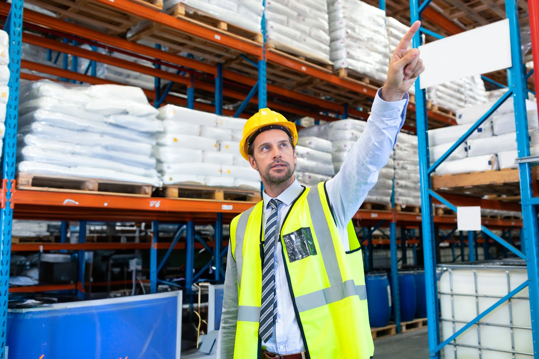 Engenheiro com colete de segurança e capacete inspecionando pallets em um armazém, avaliando organização, estoque e processos logísticos