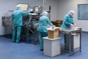 Profissionais realizando inspeção e preparação de materiais em área controlada da indústria farmacêutica, representando boas práticas de fabricação e controle de qualidade.