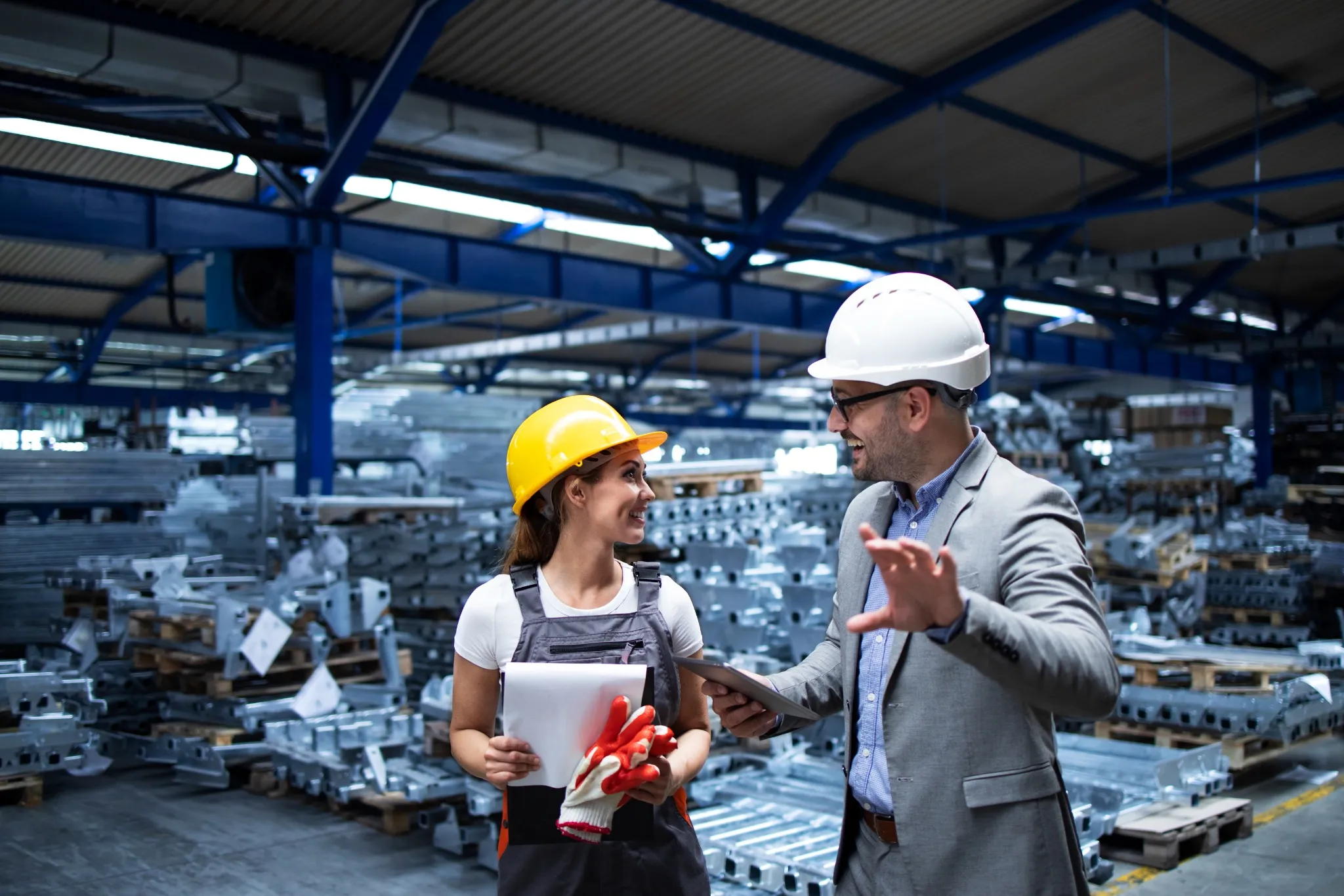 Supervisor e operadora conversando em área industrial, avaliando produção e discutindo melhorias de processos.